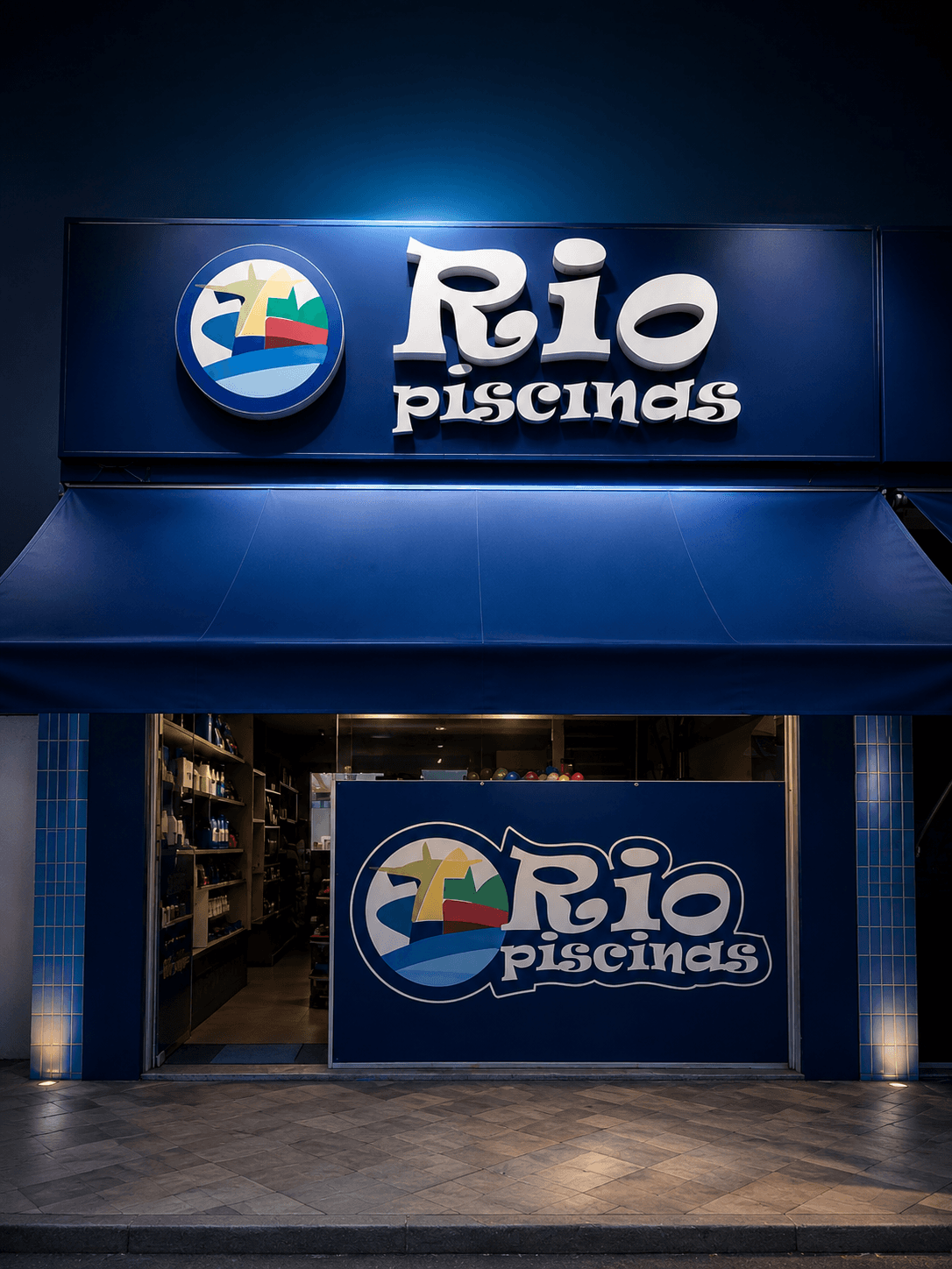 Fachada iluminada da loja Rio Piscinas à noite, com letreiro e vitrine